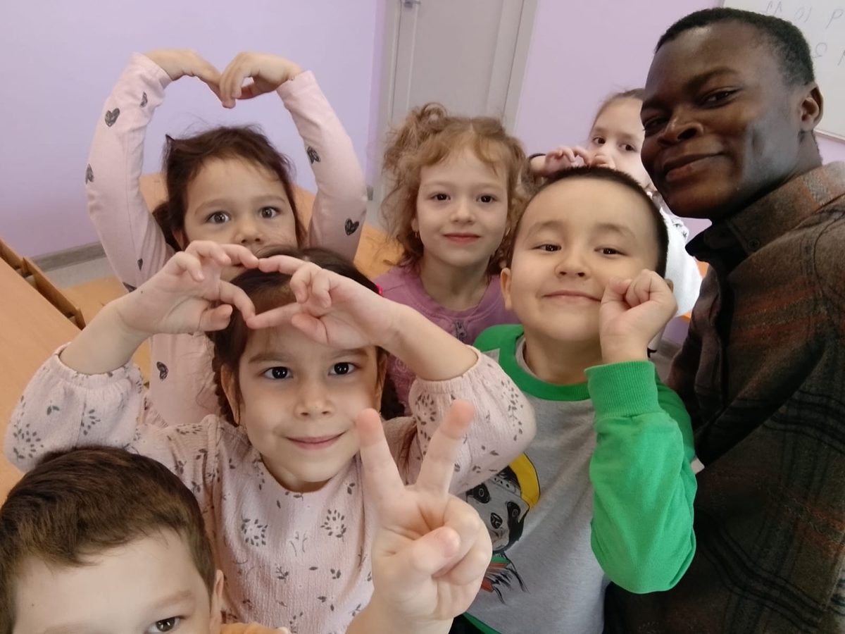 Emmanuel smiling with children making heart shapes with their hands
